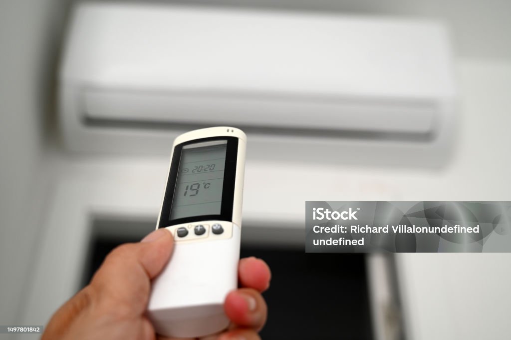 Adjusting the air conditioning temperature Adjusting the air conditioning with a remote control in hand Air Conditioner Stock Photo