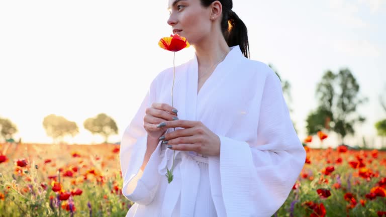 Young woman walking on meadow and enjoying by flowering poppies.