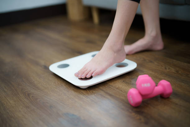 istock Fat diet and scale feet standing on electronic scales for weight control. Measurement instrument in kilogram for a diet control 1497805051