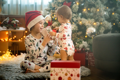 Happy boy and girl in pajamas sitting next to Christmas tree