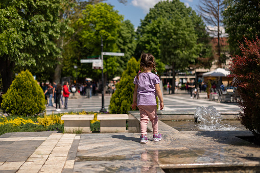 The photo of a little girl standing on a fountain.