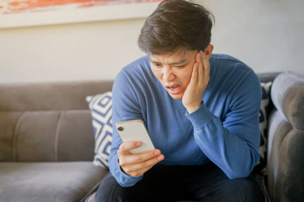 istock close up young asian man frowned on face with shock feeling while using smartphone to reading about fake news and rumor in home for people lifestyle concept 1497813099