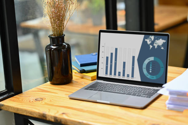 istock Laptop. computer with financial graph chart on screen snd pile of documents on wooden office desk. 1497813777