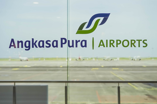 Bali, Indonesia - March 28, 2023: Angkasa Pura Airport logo on glass window with plane runaway background. Angkasa Pura is an Indonesian state-owned company or BUMN engaged in airport management.