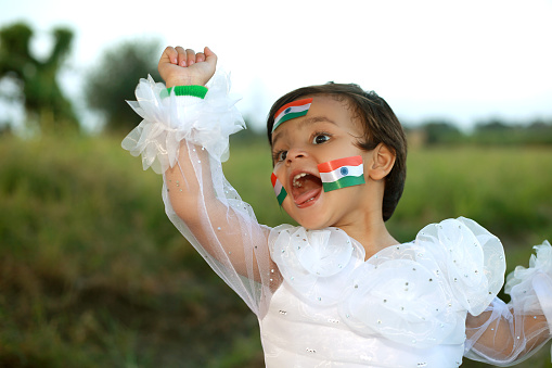 Cheerful 2-3 years girl raised hands and holding Indian flag in hand, celebrating Independence day.