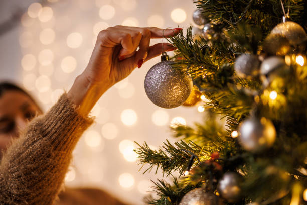 Young woman holding a basket with ornaments and decorating the Christmas tree stock photo