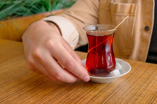 Traditional cup of Turkish black tea. A cup of Turkish tea on a saucer and a piece of sugar. A man is about to drink traditional Turkish tea.