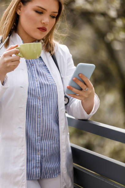 istock Young female doctor standing on the balcony, using smart phone and taking a break from work 1497823030