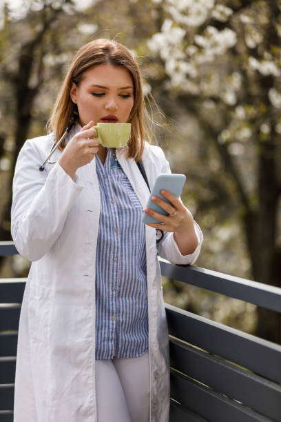 istock Young female doctor standing on the balcony, using smart phone and taking a break from work 1497823216