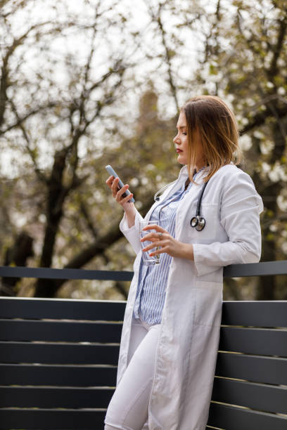 istock Young female doctor standing on the balcony, taking a break from work and using smart phone 1497823242