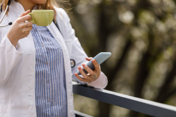istock Young female doctor standing on the balcony, using smart phone and taking a break from work 1497823367