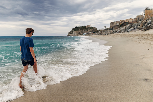 Teenage boy walking on the beach. In the distance there are cliffs of the town of Tropea.
Shot with Canon R5