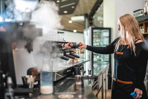 A dedicated female barista in the cafeteria exhibits true excellence, combining her passion for coffee with her creative talents, resulting in awe-inspiring latte art that leaves a lasting impression.
