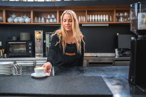 The skilled hands of a talented female barista showcase a cup of coffee in the cafeteria, embodying the artistry and dedication behind every sip.