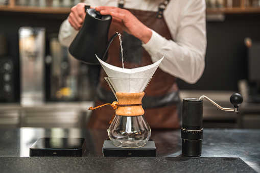 A close-up shot of a Caucasian male professional barista in a coffee house pouring water over drip coffee.