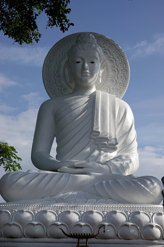 A vertical shot of a large white Zen Buddha statue against a blue sky