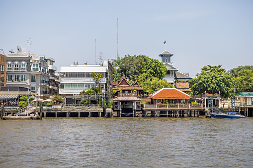 Chao Phraya River, Bangkok, Thailand - March 26th 2023: Old residential buildings at the brink of the river which runs through the capital of Thailand