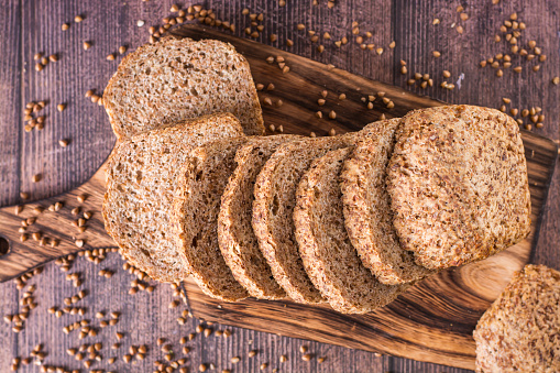 Close up of sliced buckwheat bread on a cutting board and cereals on the table top view