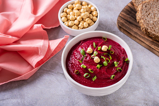 Bowl of vegetable beetroot hummus with chickpeas and herbs on the table