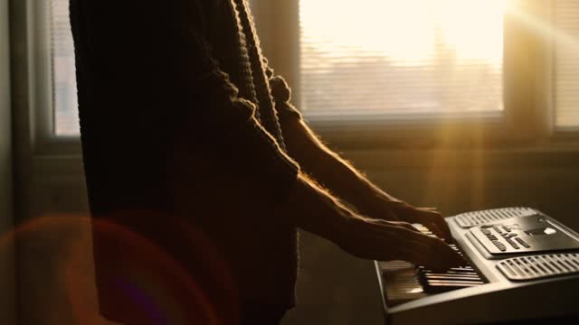 man playing synthesizer at home at sunset, music learning concept