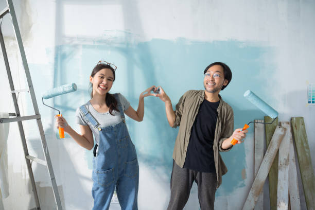 istock Asian couple expressing love heart while painting the wall with light blue paint using a roller during renovation in their new apartment. 1497831979