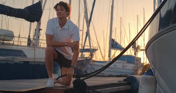 Boat, sailing and man in harbor with ropes, cable and tie knot for boating lesson, learning and leisure sport. Travel, sunset and man  on desk for cruise, luxury sailboat and adventure