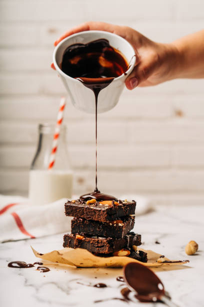 Human hand pouring melted chocolate on brownies