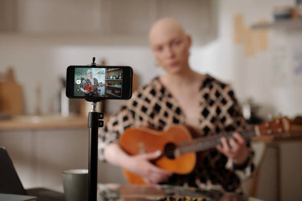 istock Focus on smartphone with young bald woman playing guitar on screen 1497843139