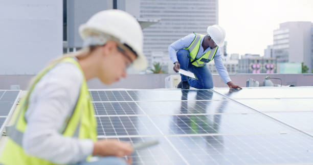 A young man writing notes while installing solar panels on the roof of a building