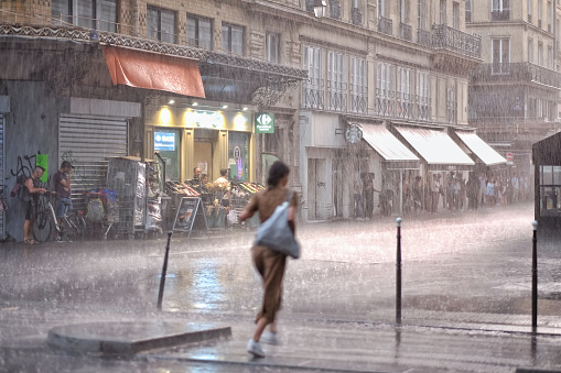 Paris, France - June 11th, 2023: A young girl running under the rain in Paris center.