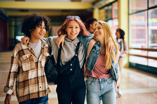 Multiracial group of happy students embracing while walking through high school hallway.