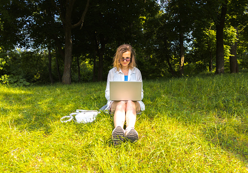 Girl with laptop working online on the nature. Remote work. Business woman is relaxing in the park.
