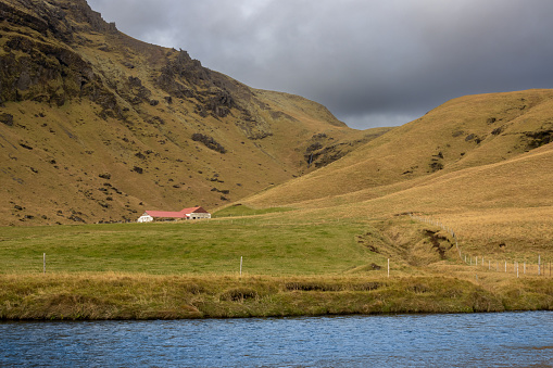 Calm bright river of a bright blue color. High mountains covered by moss and lichen in the background. Cloudy sky in the autumn. South-central Iceland.