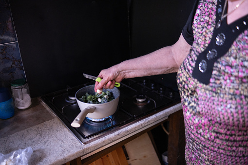 One retired woman cooking a creamy broccoli soup for her little grandchildren