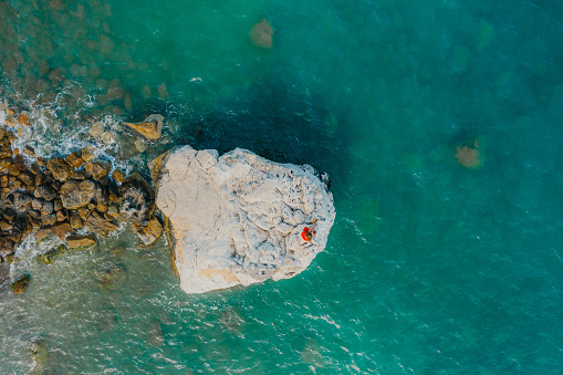Drone photo of female in bright red t-shirt relaxing on the bit rock in the sea, enjoying the scenic view of the Turkish Riviera Mediterranean landscape