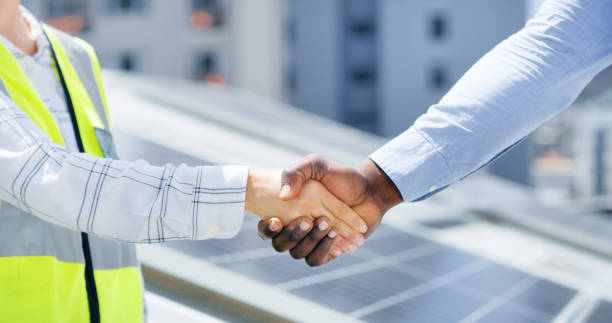 istock Closeup of hands of man and woman greeting with a handshake while installing a solar panel. Two diverse colleagues shaking hands for construction and building deal 1497853012