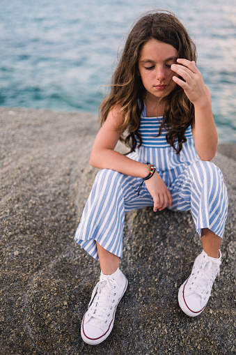 Young teenage girl sitting on a rock and enjoys the summer by the sea