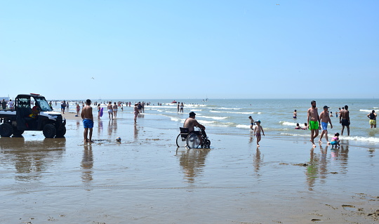 Blankenberge, West-Flanders, Belgium - June 11, 2023: lifeguard guarding from his quad. Disabled man in electric wheel chair in wet sand in front of the sea