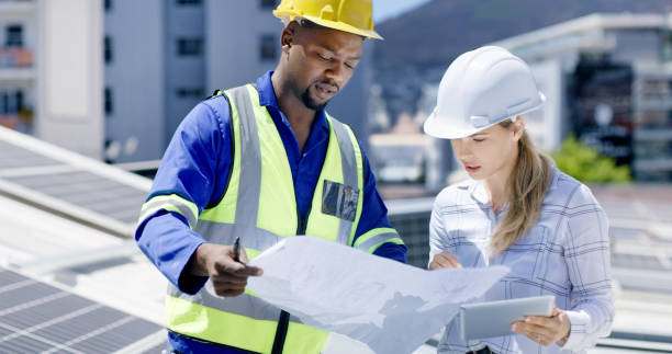 istock Engineers, architects and solar power technicians team with tablet or blueprint on building roof. Talking workers monitoring panels to harvest biodegradable energy source from sun 1497855272