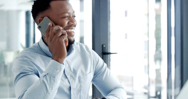 istock Happy and smiling young business man making a call using a smartphone in a modern office. Confident businessman working online with a laptop and talking on the phone at his desk 1497857439