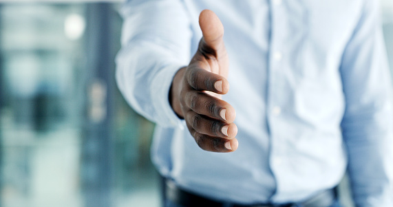 Closeup of hands of a business man reaching out for a handshake in a modern office. Businessman greeting with a welcoming gesture at a job interview