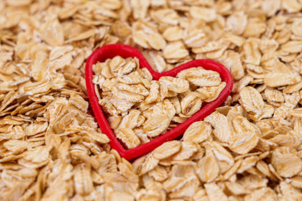 avoine de petit-déjeuner roulée crue en forme de cœur rouge. repas santé - oatmeal oat heart shape rolled oats photos et images de collection