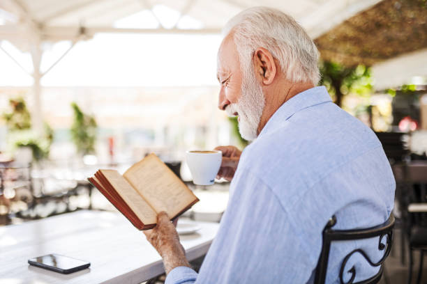 istock Smiling senior man relaxing in outdoor cafe reading book drinking coffee 1497858466