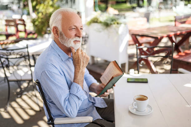 istock Smiling senior man relaxing in outdoor cafe reading book thinking 1497858476