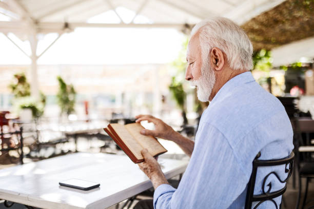 istock Senior man relaxing in outdoor cafe reading book 1497858483