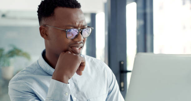 istock A young business man using a laptop and looking confused in a modern office. A businessman working online and looking unsure at his desk 1497860738