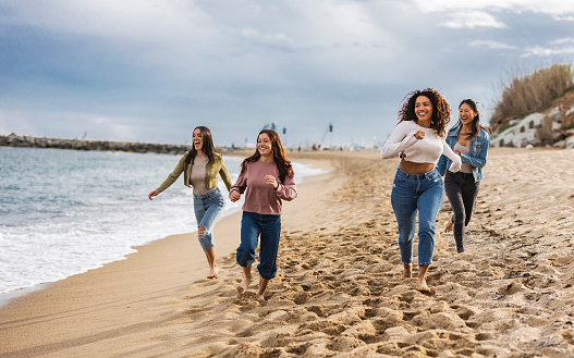 Portrait of excited young female friends running on the beach. Multiracial group of friends enjoying a day at the beach.