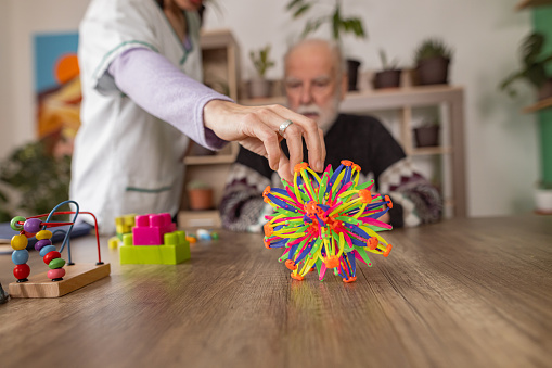 Female nurse shows elderly dementia patient how to use colorful sensory ball.