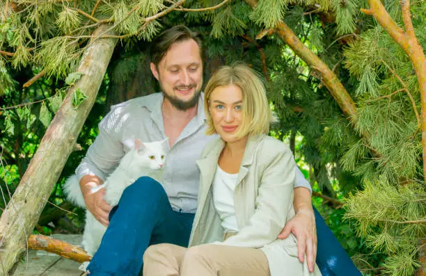 happy couple walks resting in the forest park with a white cat.portrait of a happy couple with a pet on the background of the park forest during a vacation