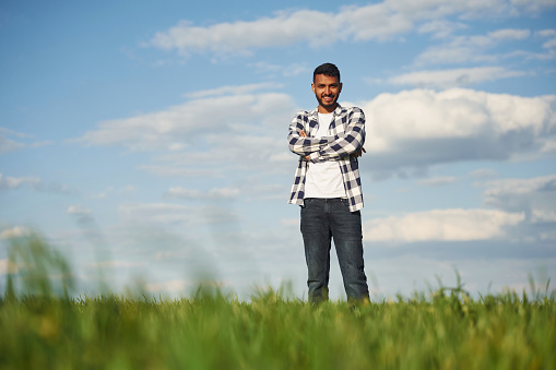 Standing with arms crossed. Handsome Indian man is on the agricultural field.